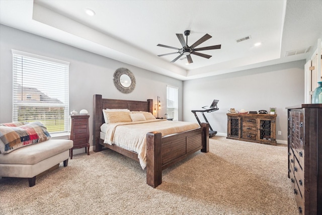 bedroom with light carpet, baseboards, visible vents, a raised ceiling, and ceiling fan