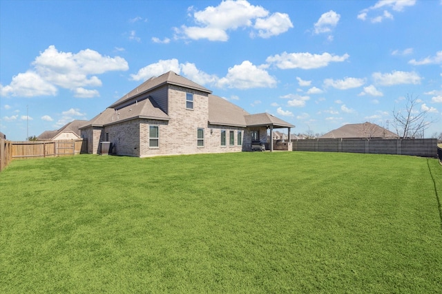 rear view of property featuring a fenced backyard, a lawn, and brick siding