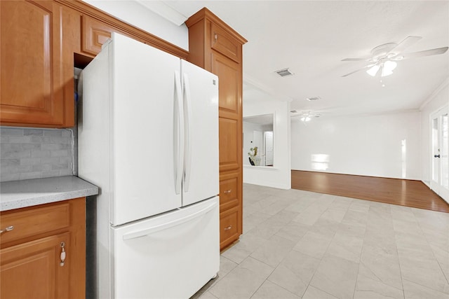 kitchen with ceiling fan, tasteful backsplash, brown cabinetry, and freestanding refrigerator