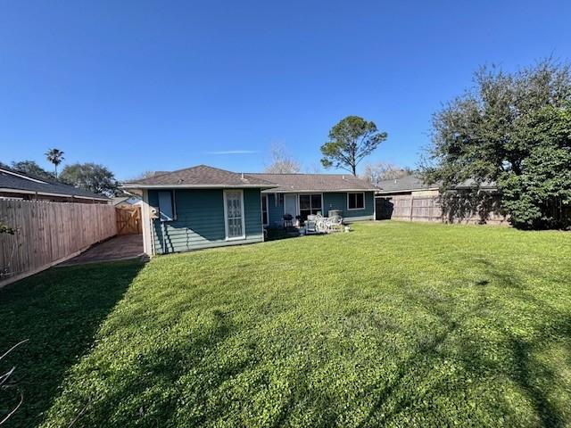 rear view of property featuring a yard and a fenced backyard