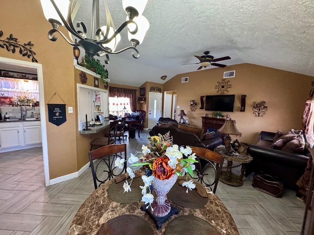 dining area featuring vaulted ceiling, a textured ceiling, ceiling fan with notable chandelier, and visible vents