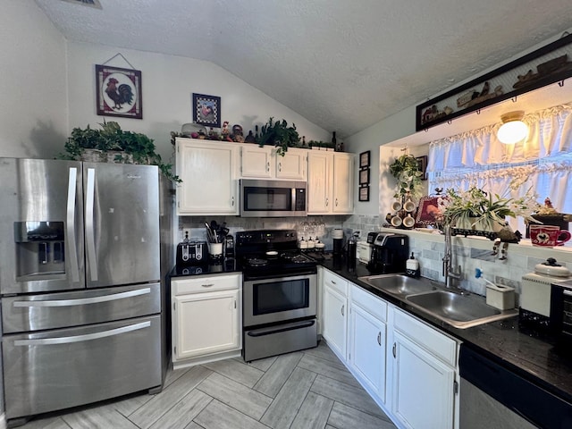 kitchen featuring stainless steel appliances, dark countertops, white cabinets, vaulted ceiling, and a sink