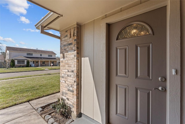 entrance to property featuring brick siding and a lawn