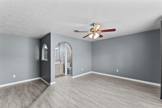 interior space featuring arched walkways, a ceiling fan, a textured ceiling, light wood-type flooring, and baseboards