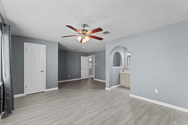 empty room with light wood-style floors, arched walkways, visible vents, and a ceiling fan