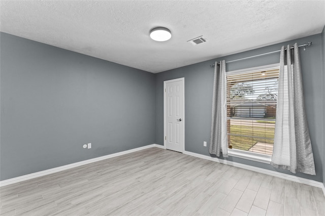 empty room featuring a textured ceiling, wood finished floors, visible vents, and baseboards