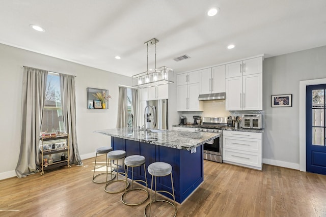 kitchen with light stone counters, under cabinet range hood, stainless steel appliances, visible vents, and a kitchen breakfast bar