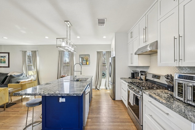 kitchen featuring visible vents, appliances with stainless steel finishes, open floor plan, under cabinet range hood, and a sink