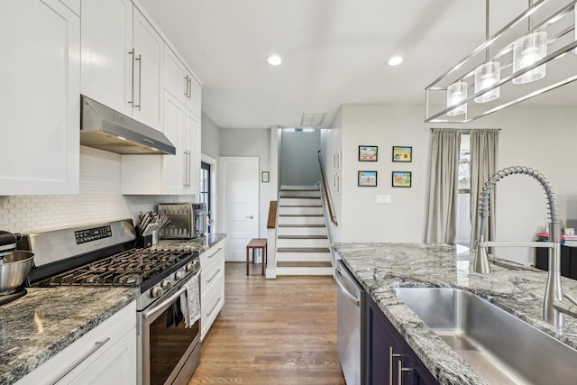 kitchen with light wood-type flooring, under cabinet range hood, white cabinets, a sink, and appliances with stainless steel finishes