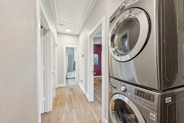 washroom featuring stacked washer / drying machine, laundry area, a textured wall, attic access, and light wood-type flooring