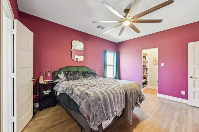 bedroom featuring a ceiling fan, visible vents, baseboards, and wood finished floors