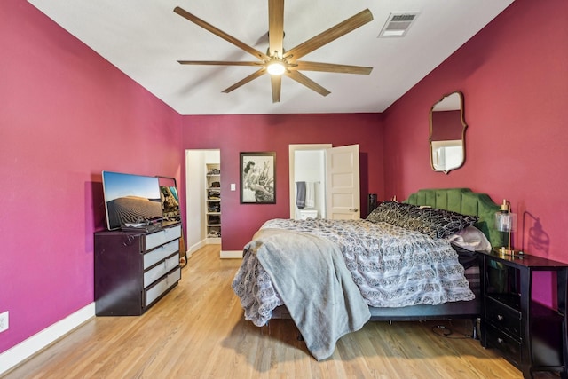 bedroom with baseboards, visible vents, a walk in closet, and wood finished floors