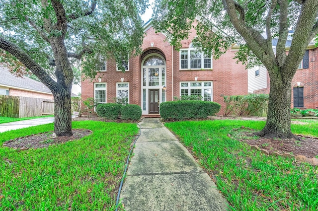 traditional-style house featuring brick siding, a front lawn, and fence