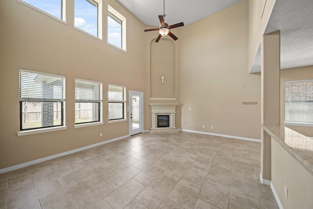 unfurnished living room featuring a ceiling fan, a glass covered fireplace, a high ceiling, light tile patterned flooring, and baseboards