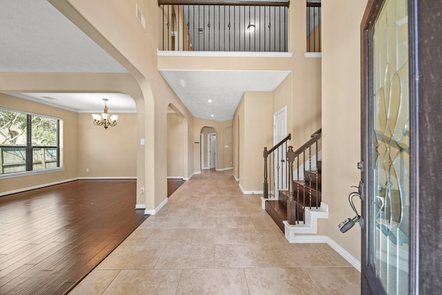 tiled entrance foyer with visible vents, arched walkways, baseboards, a chandelier, and stairs