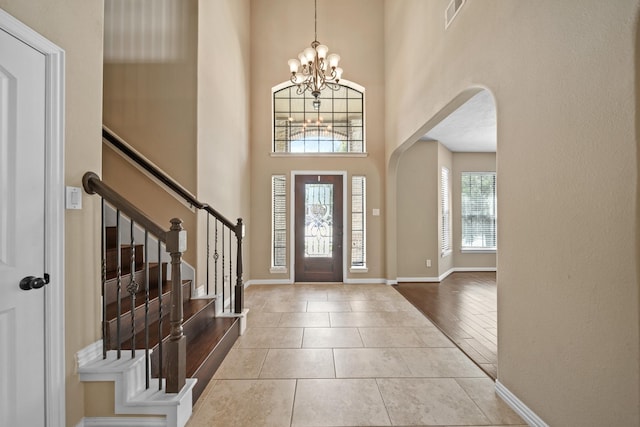 tiled entryway featuring arched walkways, a chandelier, baseboards, a towering ceiling, and stairs