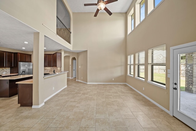 unfurnished living room featuring ceiling fan, baseboards, recessed lighting, light tile patterned flooring, and arched walkways