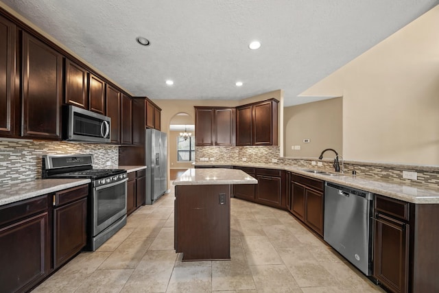 kitchen with a sink, a kitchen island, stainless steel appliances, a peninsula, and dark brown cabinets