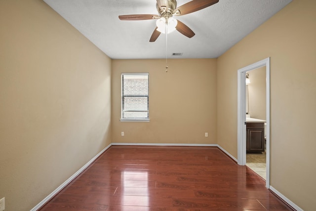 spare room featuring ceiling fan, visible vents, baseboards, and wood finished floors