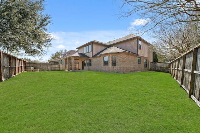 rear view of property featuring brick siding, a fenced backyard, and a yard