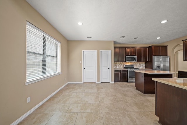 kitchen featuring tasteful backsplash, a center island, stainless steel appliances, light countertops, and dark brown cabinets