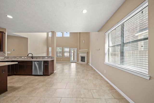 kitchen featuring tasteful backsplash, dark brown cabinetry, dishwasher, light tile patterned floors, and a glass covered fireplace