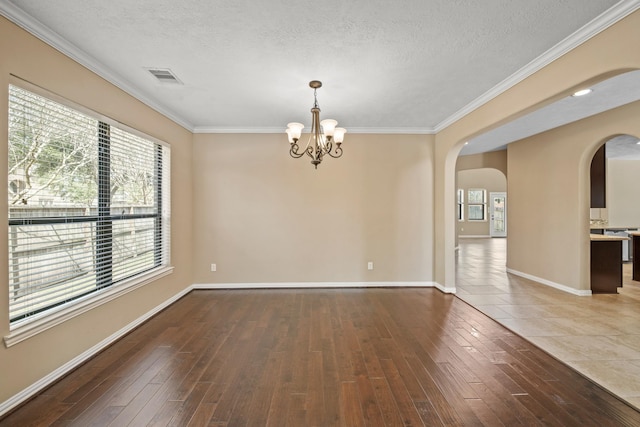 empty room featuring visible vents, arched walkways, a textured ceiling, and wood finished floors