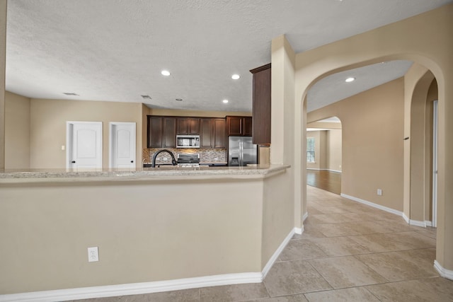 kitchen featuring backsplash, baseboards, dark brown cabinetry, appliances with stainless steel finishes, and arched walkways