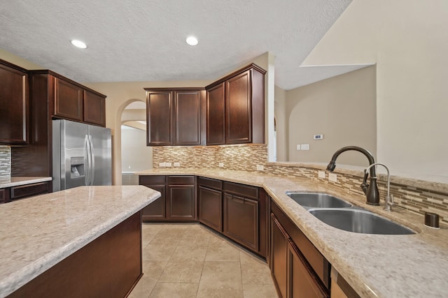 kitchen featuring backsplash, light stone counters, light tile patterned flooring, stainless steel fridge, and a sink