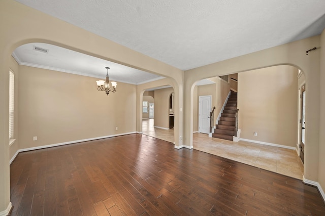 empty room with visible vents, baseboards, a chandelier, wood finished floors, and a textured ceiling