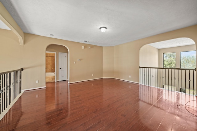 spare room featuring arched walkways, baseboards, and wood finished floors