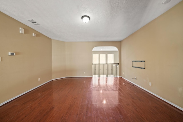 unfurnished room with wood finished floors, visible vents, baseboards, arched walkways, and a textured ceiling