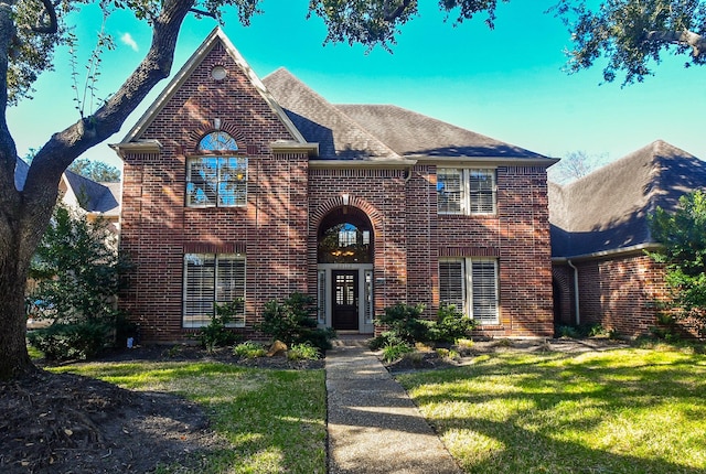 traditional home with a front yard, brick siding, and a shingled roof