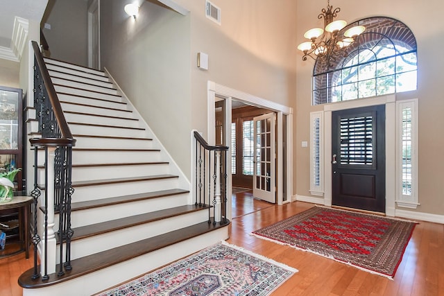 foyer featuring wood finished floors, visible vents, a towering ceiling, and a healthy amount of sunlight