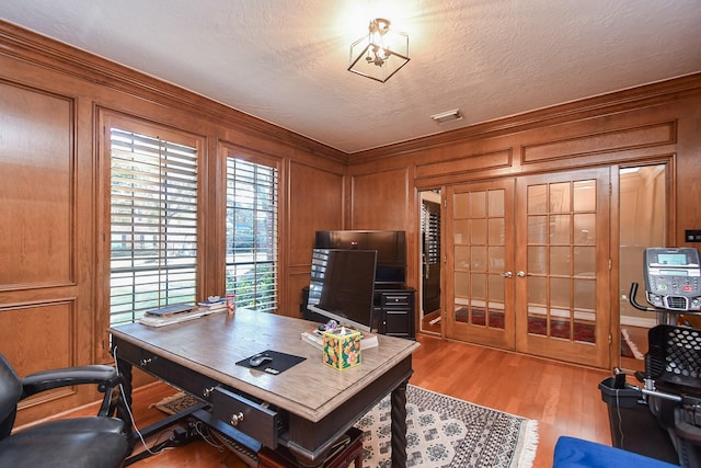 office space featuring visible vents, wood walls, light wood-style flooring, french doors, and a textured ceiling