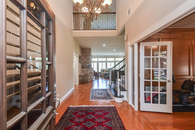 foyer with a chandelier, visible vents, a towering ceiling, and wood finished floors