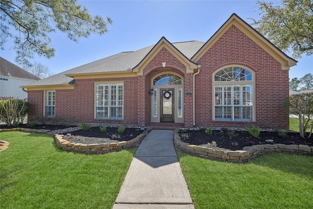 view of front facade with roof with shingles, a front lawn, and brick siding