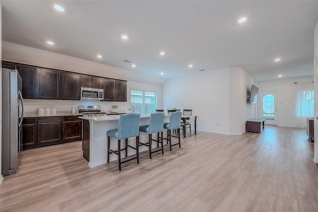 kitchen with a breakfast bar area, light wood-style flooring, appliances with stainless steel finishes, a kitchen island, and dark brown cabinets