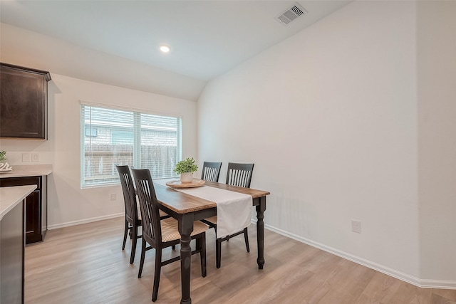 dining space featuring light wood-style floors, baseboards, visible vents, and vaulted ceiling