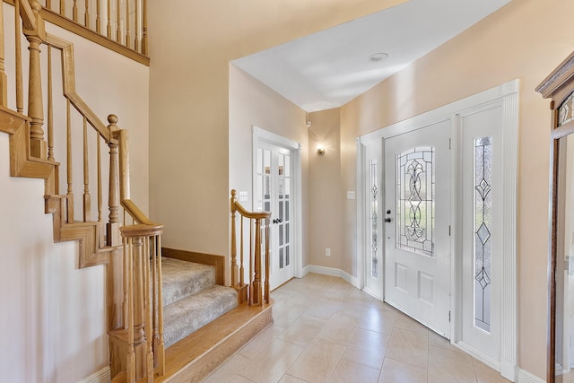 foyer entrance with light tile patterned floors, stairs, and baseboards