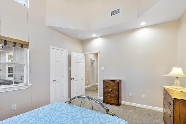 bedroom with baseboards, visible vents, light carpet, and a high ceiling