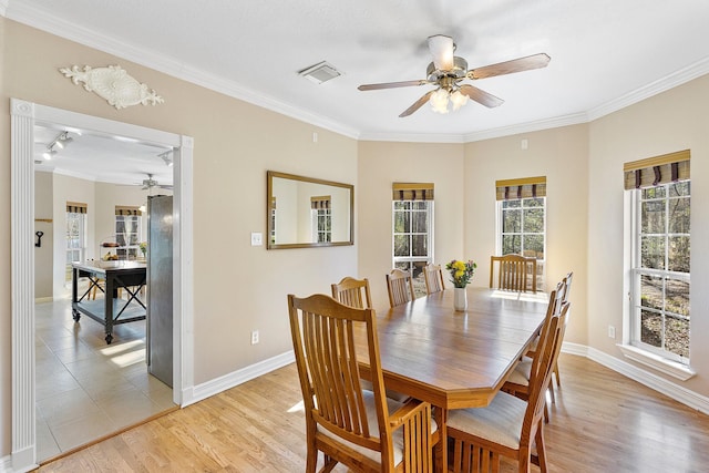 dining area featuring visible vents, light wood-style flooring, ornamental molding, a ceiling fan, and baseboards