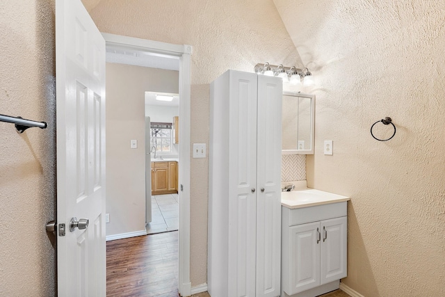 bathroom with lofted ceiling, a textured wall, vanity, and wood finished floors