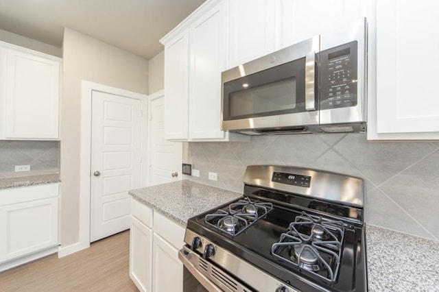 kitchen with appliances with stainless steel finishes, white cabinetry, decorative backsplash, and light stone countertops