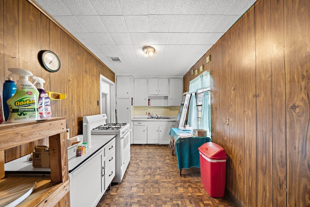 kitchen with white gas range, visible vents, white cabinetry, a sink, and wooden walls