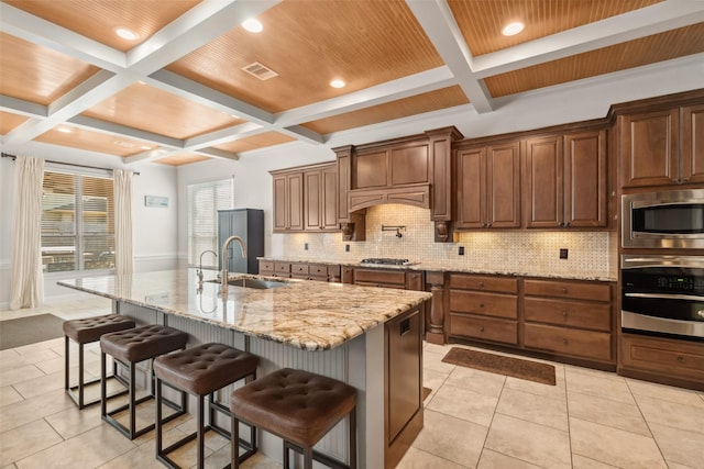 kitchen featuring a breakfast bar, coffered ceiling, a sink, appliances with stainless steel finishes, and backsplash