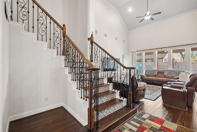 staircase with high vaulted ceiling, wood-type flooring, baseboards, and crown molding