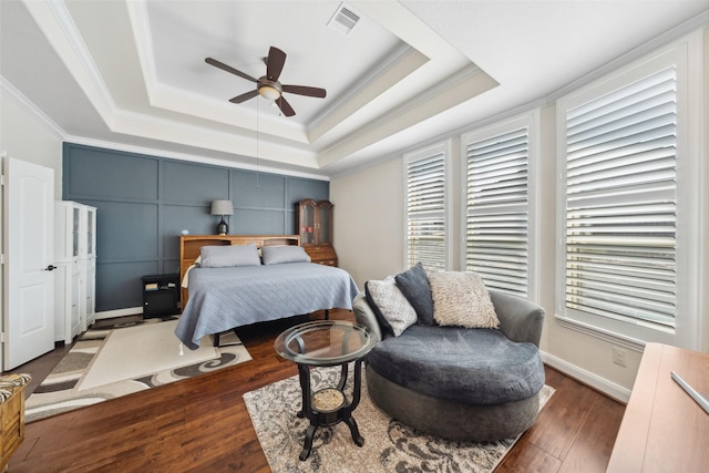 bedroom with visible vents, a tray ceiling, wood-type flooring, and ornamental molding