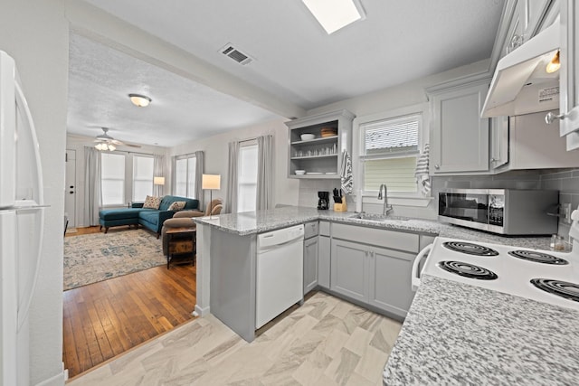 kitchen featuring visible vents, a sink, a peninsula, white appliances, and under cabinet range hood