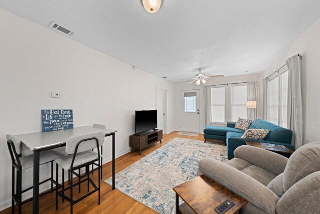 living area with a ceiling fan, wood finished floors, visible vents, and baseboards